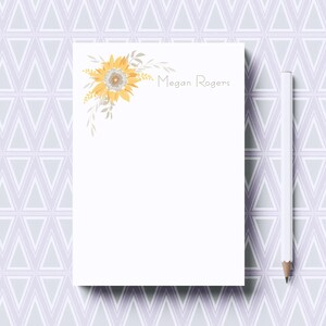 May include: A white notepad with a sunflower illustration and the name "Megan Rogers" printed at the top. The notepad is on a light purple background with a geometric pattern.