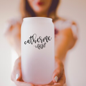 May include: A frosted glass can-shaped tumbler with the name "Catherine" in elegant black script, accompanied by a small botanical illustration. The glass is held up, showcasing the design.