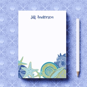 May include: A white notepad with a blue seashell design at the bottom. The notepad has the name "Jill Anderson" printed at the top.