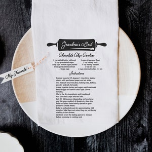 May include: A white tea towel with a black and white illustration of a rolling pin and the text "Grandma's Best Chocolate Chip Cookies". The recipe is printed below the illustration, including ingredients and instructions.