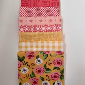 May include: A selection of fabric swatches with diverse patterns and colours. Designs include floral, gingham, bee, and text prints in pink, yellow, and white. The text includes phrases such as "May Good Things" and "the wild things are".