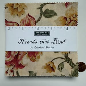 May include: A stack of fabric squares with a floral pattern in cream, red, yellow, and green. The fabric is labeled "Threads that Bind" by Blackbird Designs. A ruler is placed on top of the fabric squares.