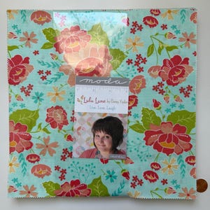 May include: A square piece of fabric with a floral pattern in red, pink, and green on a light blue background. The fabric features various flower designs. A small card with the text "Lulu Lane by Corey Yoder" is attached.