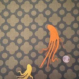 Może przedstawiać: Tkanina z powtarzającym się wzorem oliwkowych czterolistnych koniczyn i kół na ciemnoszarym tle. Widoczne są dwie pomarańczowe ilustracje ośmiornic i jedna żółta ilustracja ośmiornicy. Widoczna jest również amerykańska moneta.