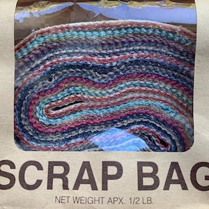 Może przedstawiać: Zwinięty pakiet kolorowych skrawków materiału w przezroczystej plastikowej torbie. Tkanina zawiera mieszankę odcieni niebieskiego, różowego, turkusowego i szarego. Torba jest oznaczona napisem "SCRAP BAG".