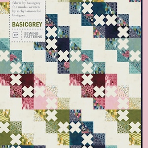 May include: A patchwork quilt with a repeating pattern of white crosses and colorful squares. The squares feature floral, geometric, and solid designs in shades of pink, green, blue, and burgundy. The quilt has the text "STOLEN KISSES PAT011" and "BASICGREY".