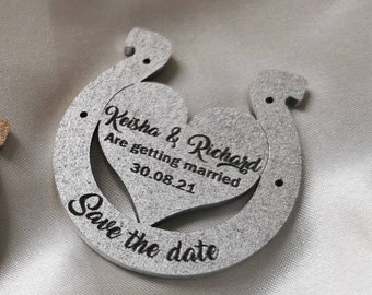 May include: Two wooden horseshoe-shaped save the date cards. One is gold and the other is silver. Both cards have the text "Keisha & Richard Are getting married 30.08.21 Save the date" engraved on them.