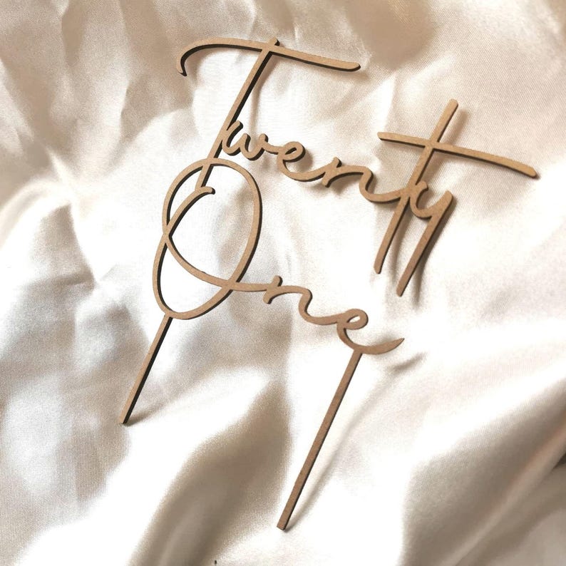 May include: Wooden cake topper with the words "Twenty One" written in a cursive script.