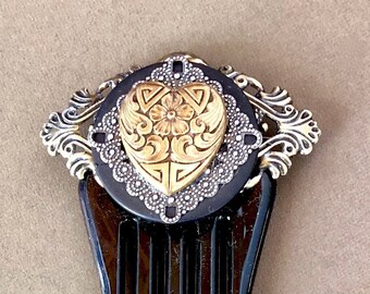 May include: A black tortoiseshell hair comb with a decorative silver and gold heart-shaped ornament. The ornament features a floral design.