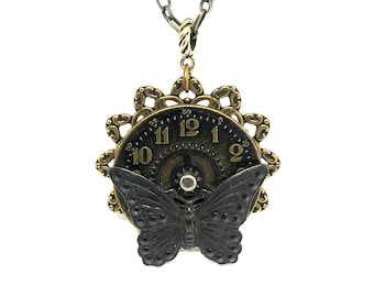 May include: A gold chain necklace with a black butterfly pendant. The pendant features a clock face with Roman numerals and a gear design.