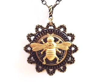 May include: A gold bee pendant necklace with a black chain. The bee is surrounded by a circular, ornate, brass frame with gears.
