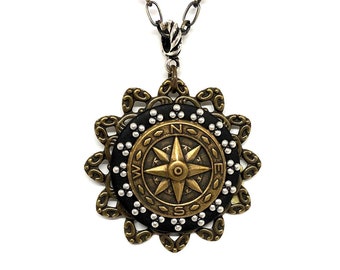 May include: A gold and silver compass pendant necklace with a black background and white dots around the compass. The necklace has a silver chain.