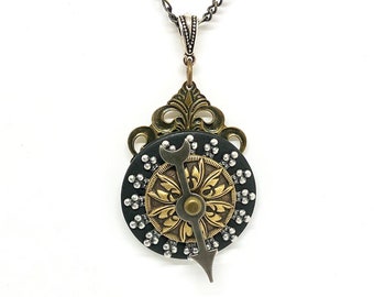 May include: A silver chain necklace with a black and gold pendant. The pendant features a circular design with a gold gear and a silver arrow.