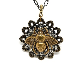 May include: A gold bee pendant necklace with a black chain. The bee is surrounded by a silver filigree design with white pearl accents.