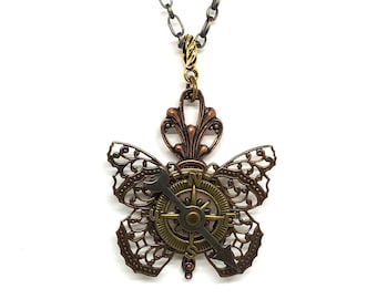 May include: A bronze and gold butterfly necklace with a compass in the center. The compass has a black face with gold accents and a silver needle. The butterfly wings are detailed and intricate.