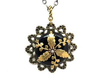 May include: A black and gold necklace with a round pendant featuring a floral design. The pendant is surrounded by a decorative filigree frame.