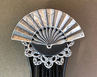 May include: A black hair comb with a silver fan-shaped design on top. The fan has a detailed design and is attached to a black base with a silver filigree border.