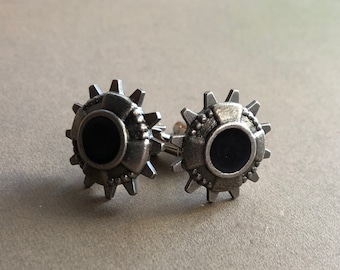 May include: A pair of silver cufflinks with black enamel insets, shaped like gears.