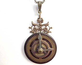 May include: Steampunk-style pendant necklace featuring a circular clock design with visible gears and hands. The pendant has a bronze finish and hangs from a matching chain. The clock face is dark brown with gold-colored gears and hands.