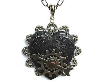 May include: A black heart-shaped pendant with intricate carvings and a silver gear and arrow design. The pendant is attached to a silver chain.