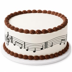 May include: A round cake with smooth white frosting, decorated with a border of brown chocolate icing swirls along the top and bottom edges. The side of the cake features a black printed musical staff with a treble clef and various notes.