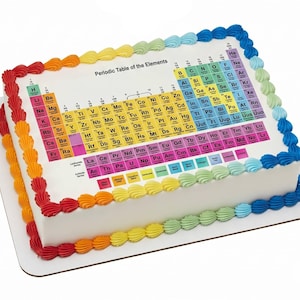 May include: A rectangular white cake decorated with a colorful Periodic Table of the Elements design. The cake is edged with rainbow-colored frosting, with the text "Periodic Table of the Elements" visible on top.