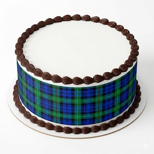 May include: A round cake with white frosting and a chocolate frosting border. The cake is decorated with a blue, green, and black plaid pattern around the sides. The cake sits on a white cake board.