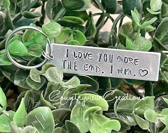 May include: Silver keychain with a rectangular tag that reads "I love you more than the end. I win." with a heart symbol.