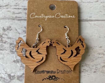 May include: A pair of wooden chicken earrings with a cutout design. The earrings are brown and have silver hooks. The earrings are displayed on a brown card with the text "Countryview Creations".