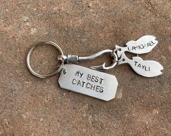 May include: Silver keychain with a fish hook charm and two fish charms with the names "Lamichal" and "Tayli" engraved on them. The keychain also has a tag that says "My Best Catches".