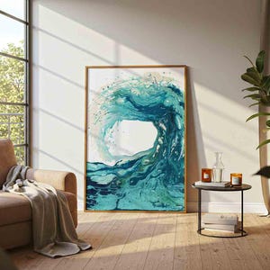 May include: A rectangular wall art print featuring an abstract fluid painting of a large ocean wave in shades of teal, turquoise, and deep blue. The artwork is enclosed in a thin, light-colored wooden frame and displayed on a plain wall.