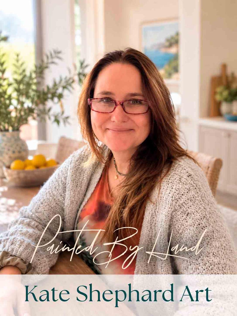 May include: A person with long brown hair wearing red-rimmed glasses, a grey textured cardigan, and an orange patterned top. The image features the text "Painted By Hand" in a cursive script and "Kate Shephard Art" in a dark serif font below.