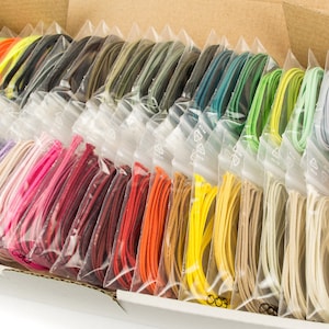 Może przedstawiać: Pudełko wypełnione małymi plastikowymi torebkami zawierającymi kolorowe sznurki. Sznurki są ułożone w rzędach według koloru, z różnymi odcieniami niebieskiego, fioletowego, różowego, czerwonego, pomarańczowego, żółtego, zielonego, brązowego i białego.