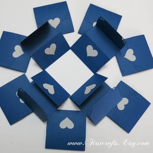 May include: A blue paper explosion box with white hearts cut out. The box is folded flat and ready to be assembled. The box is decorated with the text "www.Firstcrafts.Etsy.com".