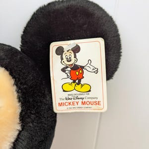 Puede incluir: Un juguete de peluche de Mickey Mouse con un dise&ntilde;o en blanco y negro. El juguete tiene una etiqueta que dice "Hecho exclusivamente para The Walt Disney Company Mickey Mouse &copy; The Walt Disney Company".