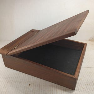 May include: A wooden box with a hinged lid, the lid is open revealing a black felt interior. The box is made of dark wood with a natural grain.