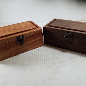May include: Two wooden boxes with hinged lids and brass clasps. The box on the left is a light brown wood, while the box on the right is a dark brown wood.
