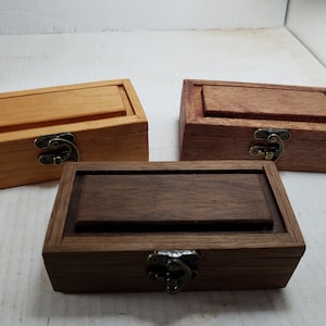May include: Three wooden boxes with hinged lids and brass clasps. The boxes are made of different types of wood: light wood, dark wood, and a reddish brown wood.