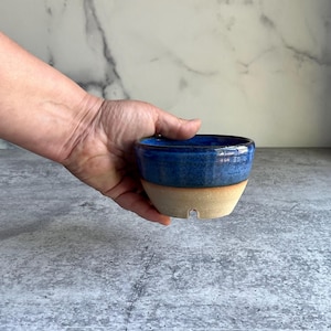May include: A small, blue and beige ceramic planter with a drainage hole. The planter is handmade and has a rustic, earthy look.