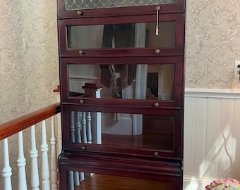 May include: A tall, dark wood barrister bookcase featuring five stacked compartments with glass doors. The top section has leaded glass panes, while the four lower sections have clear glass panels, each equipped with a small round wooden knob.