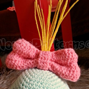 May include: A crocheted hat with a pink bow and yellow yarn strands on top. The hat is light blue and green.