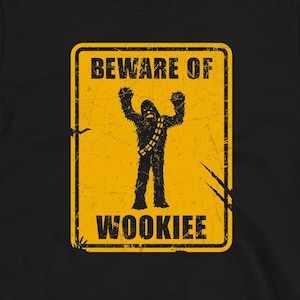 May include: Black t-shirt featuring a yellow warning sign that reads "Beware of Wookiee" with a silhouette of Chewbacca inside the sign.