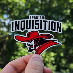 May include: A sticker with the words "SPANISH INQUISITION" in white letters on a black background. The sticker features a red-hatted figure with a stern expression. The website address www.paulsimic.com is at the bottom.