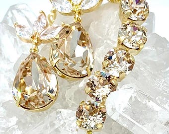 May include: A pair of gold-toned earrings featuring large, pear-shaped champagne-colored crystals suspended from marquise-cut clear stones. A curved line of round, champagne-colored crystals follows the side of the earring design.