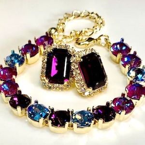 May include: A gold bracelet with alternating purple and blue gemstones. The bracelet has a clasp closure. Two matching purple gemstone earrings are also included.