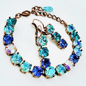 Puede incluir: Un conjunto de pulsera y pendientes de cobre con piedras de cristal azules y turquesas. La pulsera tiene un efecto degradado ombré, con las piedras volviéndose más oscuras en color a medida que bajan por la pulsera. Los pendientes son simples tachuelas con una sola piedra de cristal.