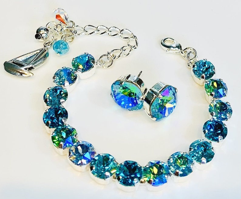Puede incluir: Un brazalete de plata con un dije de velero y un par de aretes a juego. El brazalete est&aacute; adornado con cristales azules iridiscentes.