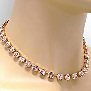 Puede incluir: Un collar tipo gargantilla en tono oro rosa que presenta una hilera de cristales redondos facetados de color rosa claro, engastados en garras metálicas individuales. El collar sigue un camino circular alrededor del cuello.