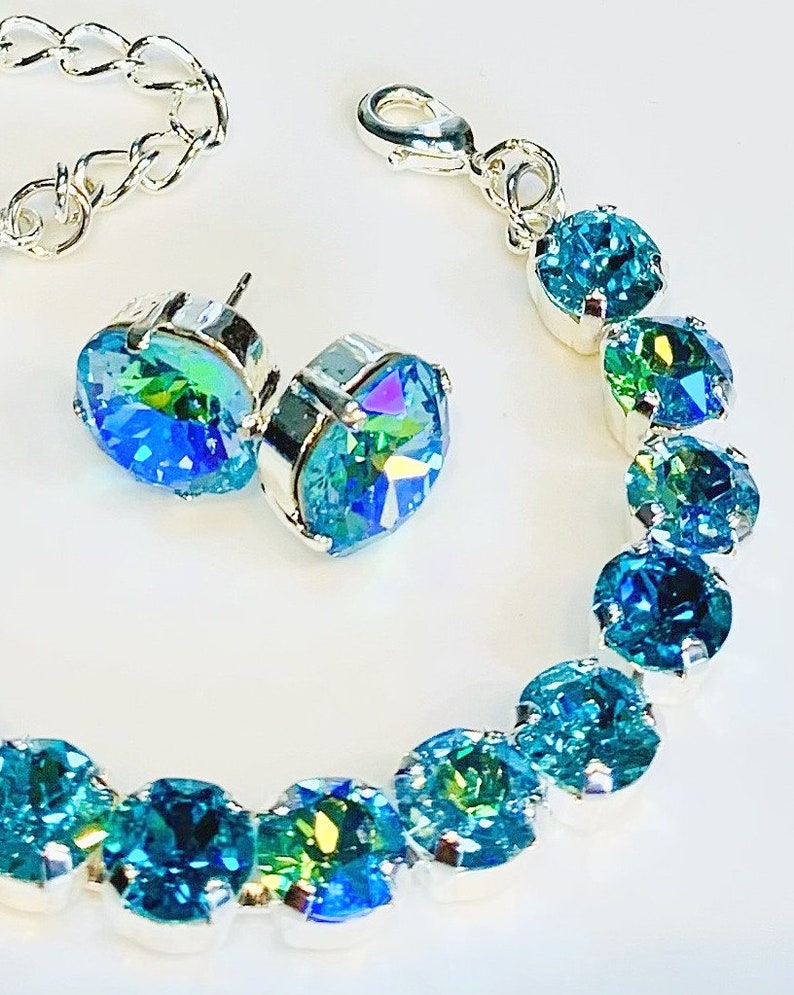 Puede incluir: Un conjunto de pendientes y pulsera de cristal iridiscente azul y verde. La pulsera est&aacute; hecha de cadena de plata y tiene un cierre de langosta.