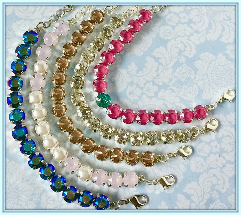 May include: A set of six bracelets with different colored crystal beads. The bracelets are made with silver chain and have a lobster clasp closure. The colors of the beads are teal, pink, white, brown, light brown, and clear.